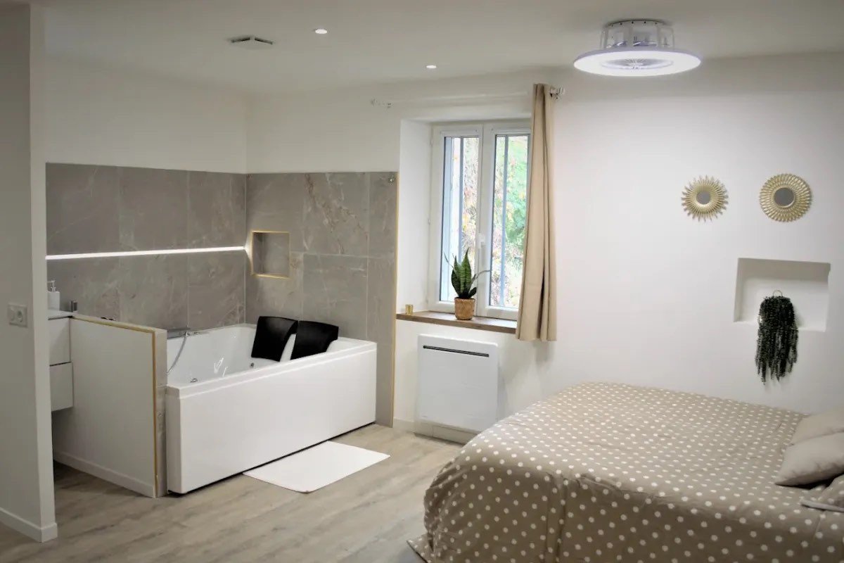 Chambre avec espace bain intégré : baignoire balnéo, faïence effet pierre et sol stratifié