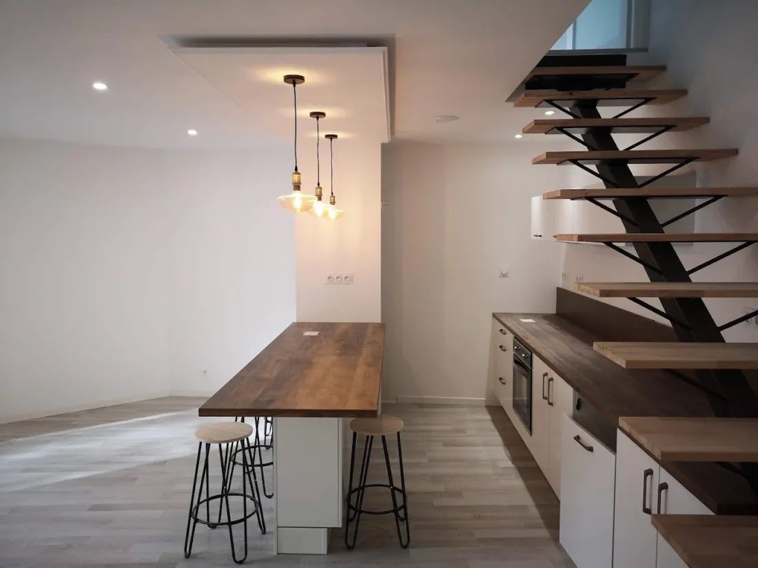 Cuisine blanche avec plan de travail bois, table haute et escalier métal et bois