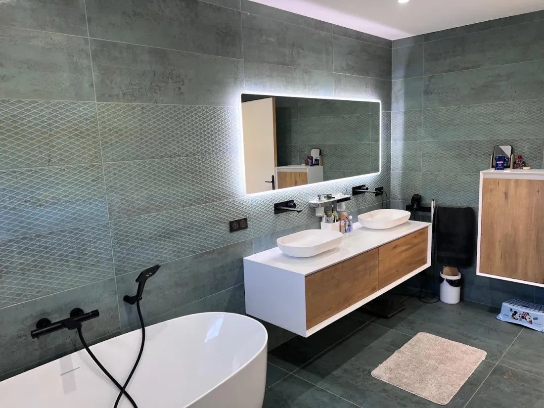 Salle de bain effet béton avec double vasque, miroir rétroéclairé et baignoire îlot
